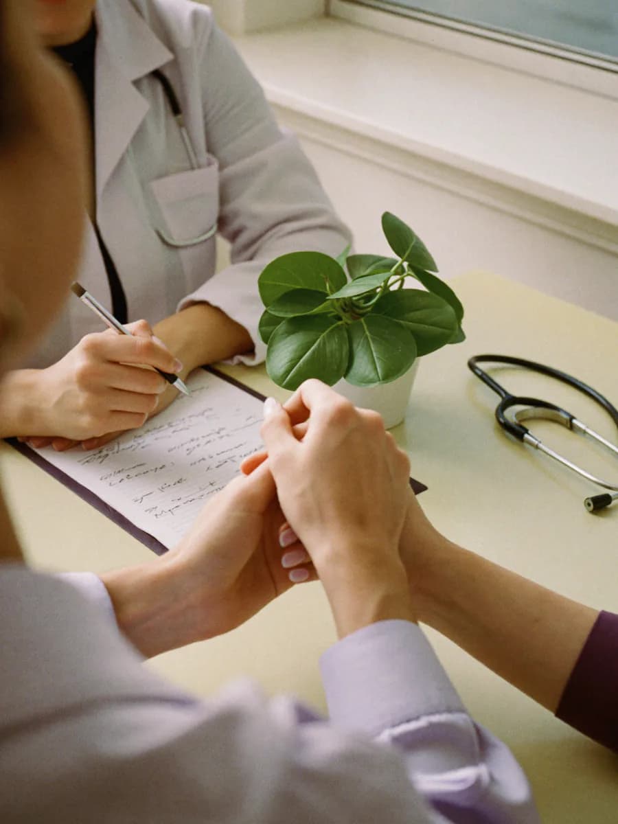 Les mains d'une médecin et de sa patiente de part et d'autre d'un bureau, un stéthoscope posé à côté du dossier